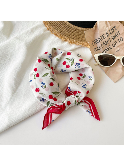 Cherry print square scarf tied in a loose knot with red border ends