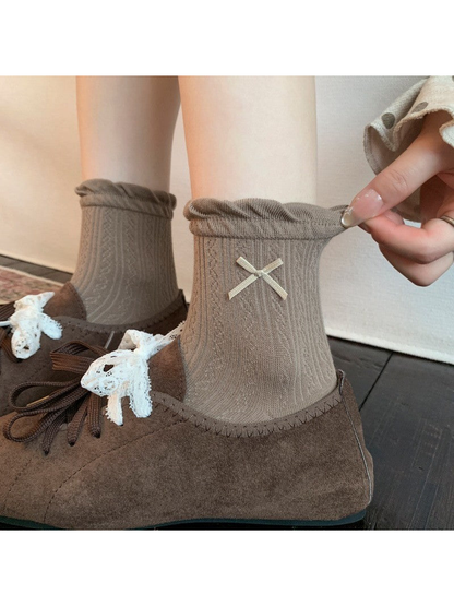 Brown ankle socks with ruffled cuffs and ribbon bows worn with brown lace-up shoes