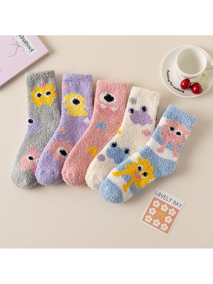 Five colorful cartoon-motif crew sock styles arranged with tabletop props