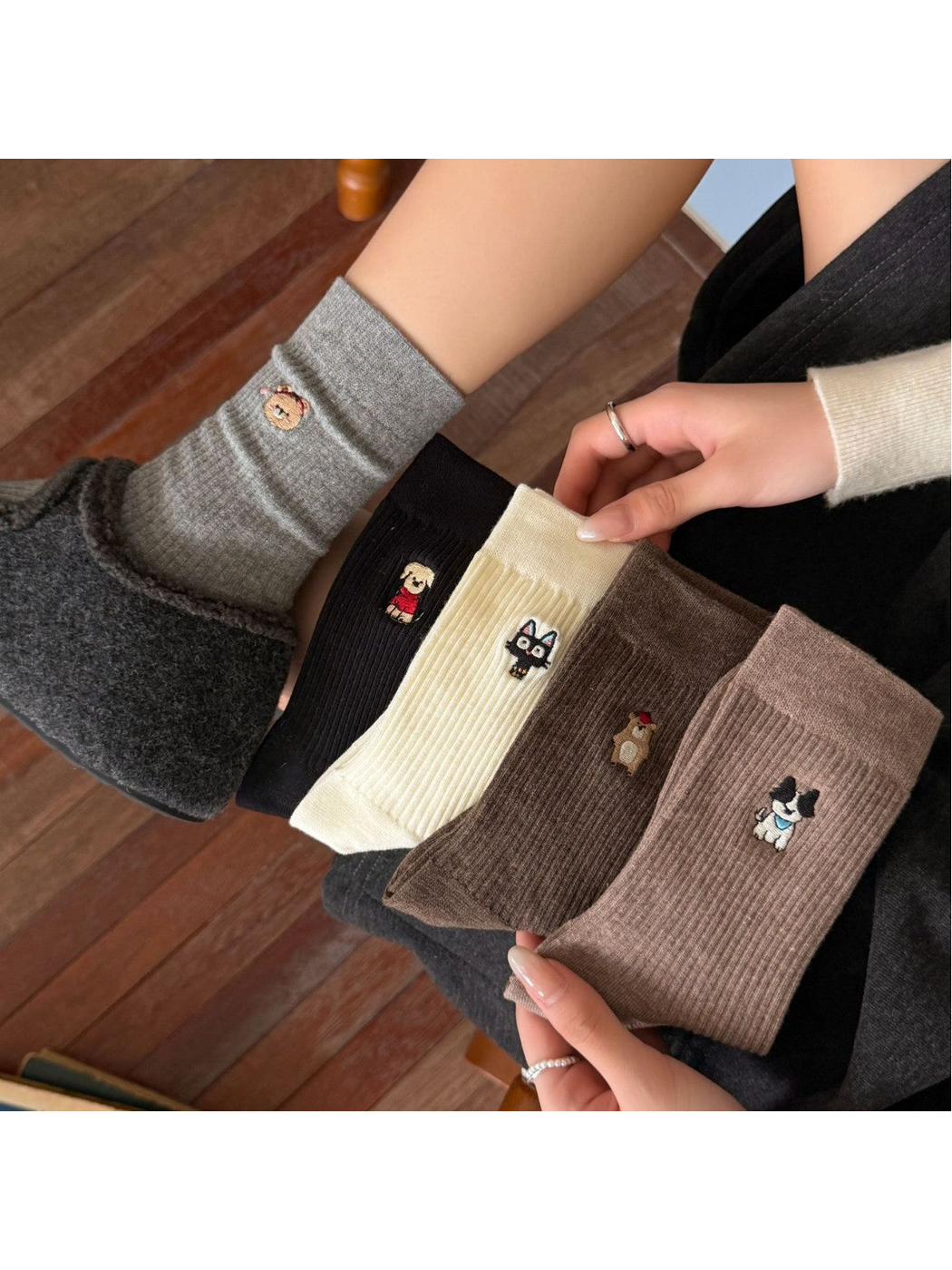 Five embroidered animal crew sock styles displayed in a seated lifestyle setting