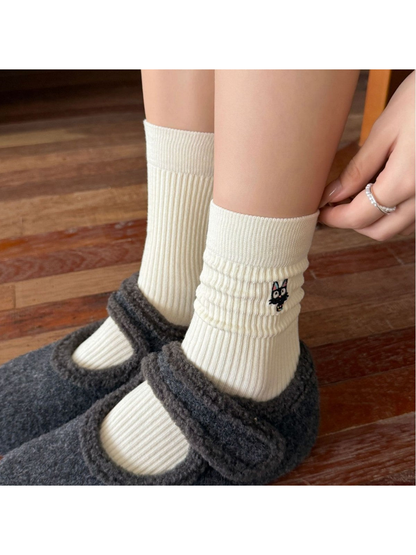 Ivory ribbed crew socks with an embroidered black cat motif worn with gray shoes
