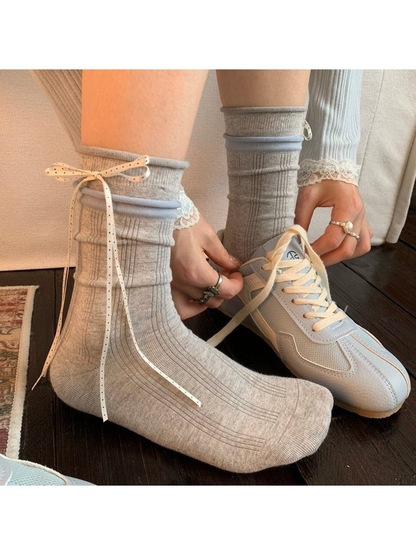 Light gray ribbed crew socks with ribbon bows worn beside a neutral sneaker