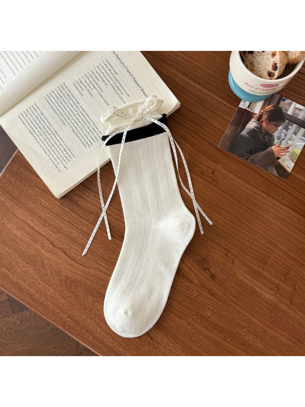 White crew sock with black contrast cuff and long ribbon ties styled beside a book and cup