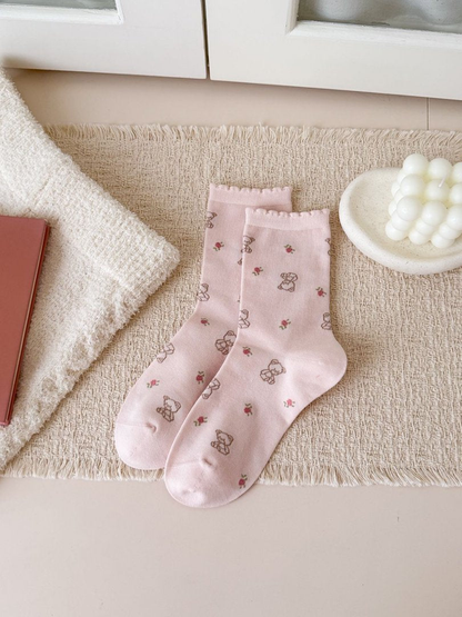 Light pink crew socks with outlined teddy bears, small flowers and ruffled cuffs