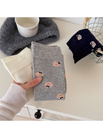 Light Gray and Ivory bear-face socks held beside folded Navy socks