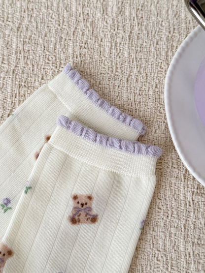 Close-up of ruffled lavender cuffs and teddy bear print on ivory socks