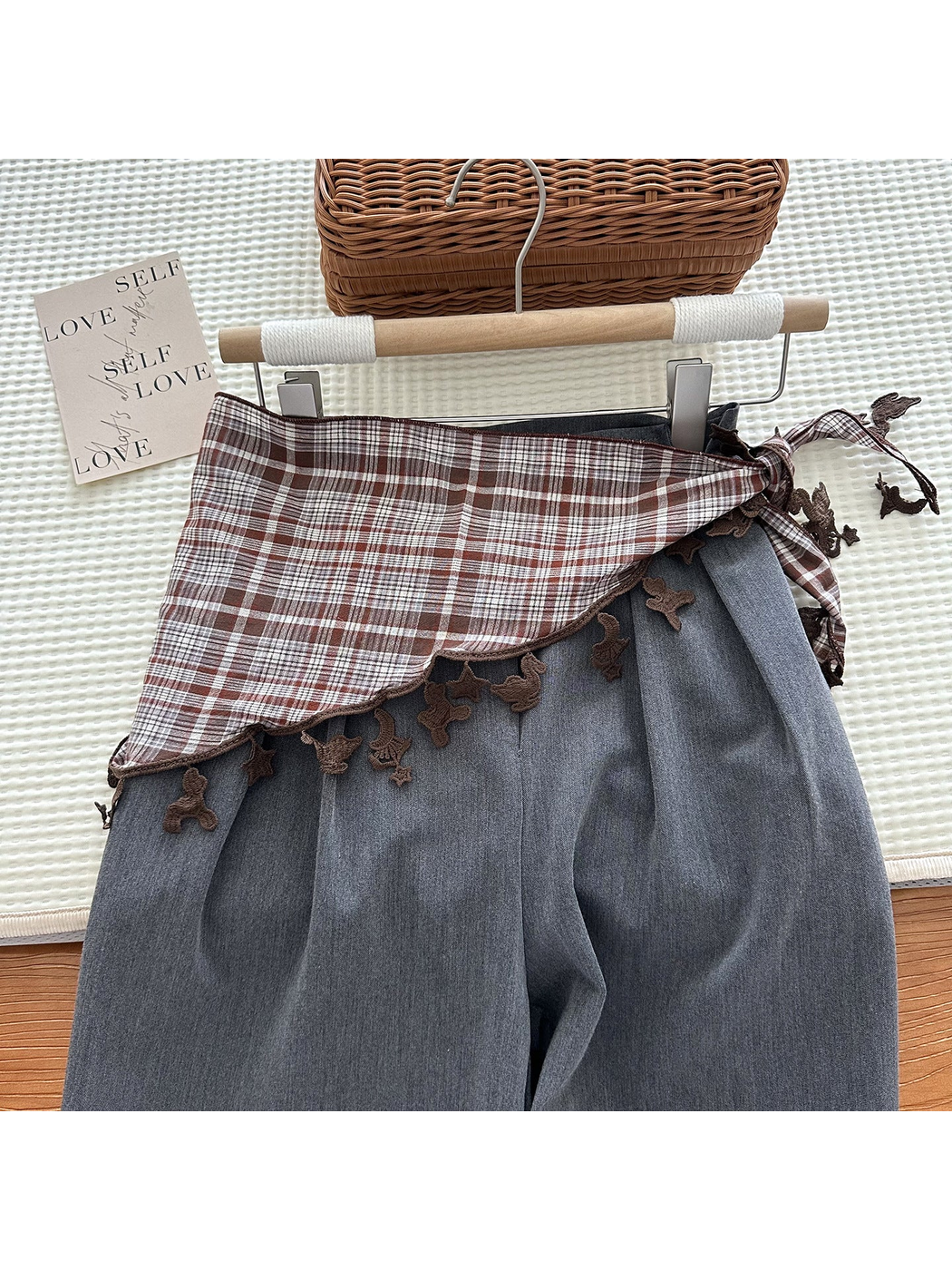 Brown plaid triangle scarf tied over gray trousers