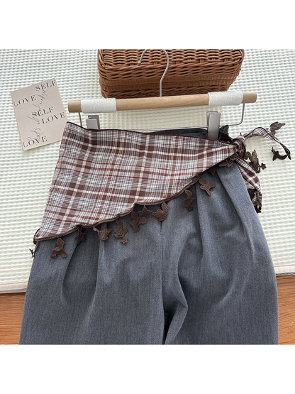 Brown plaid triangle scarf tied over gray trousers
