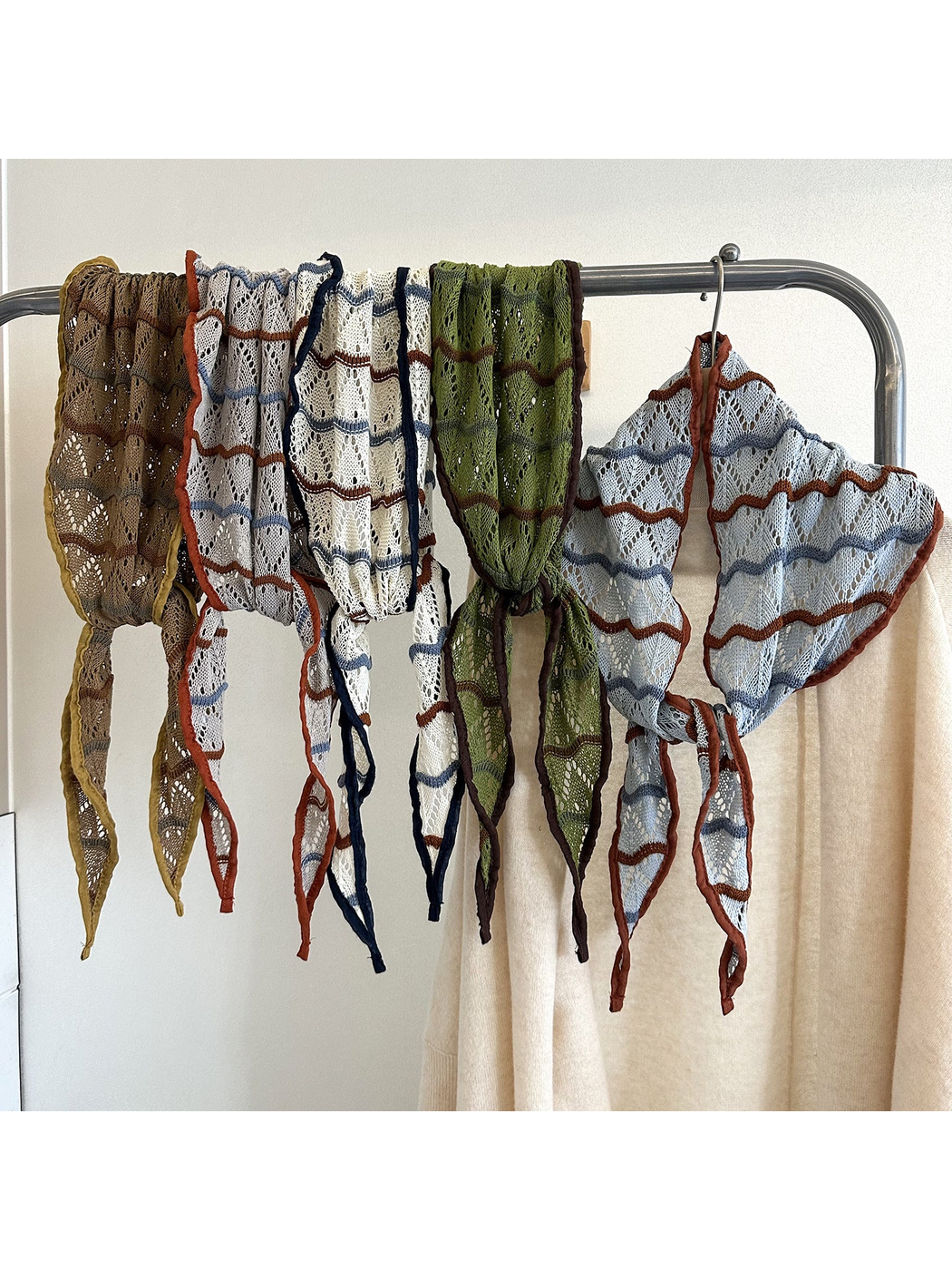 Openwork triangle scarves in five colors displayed on a garment rack