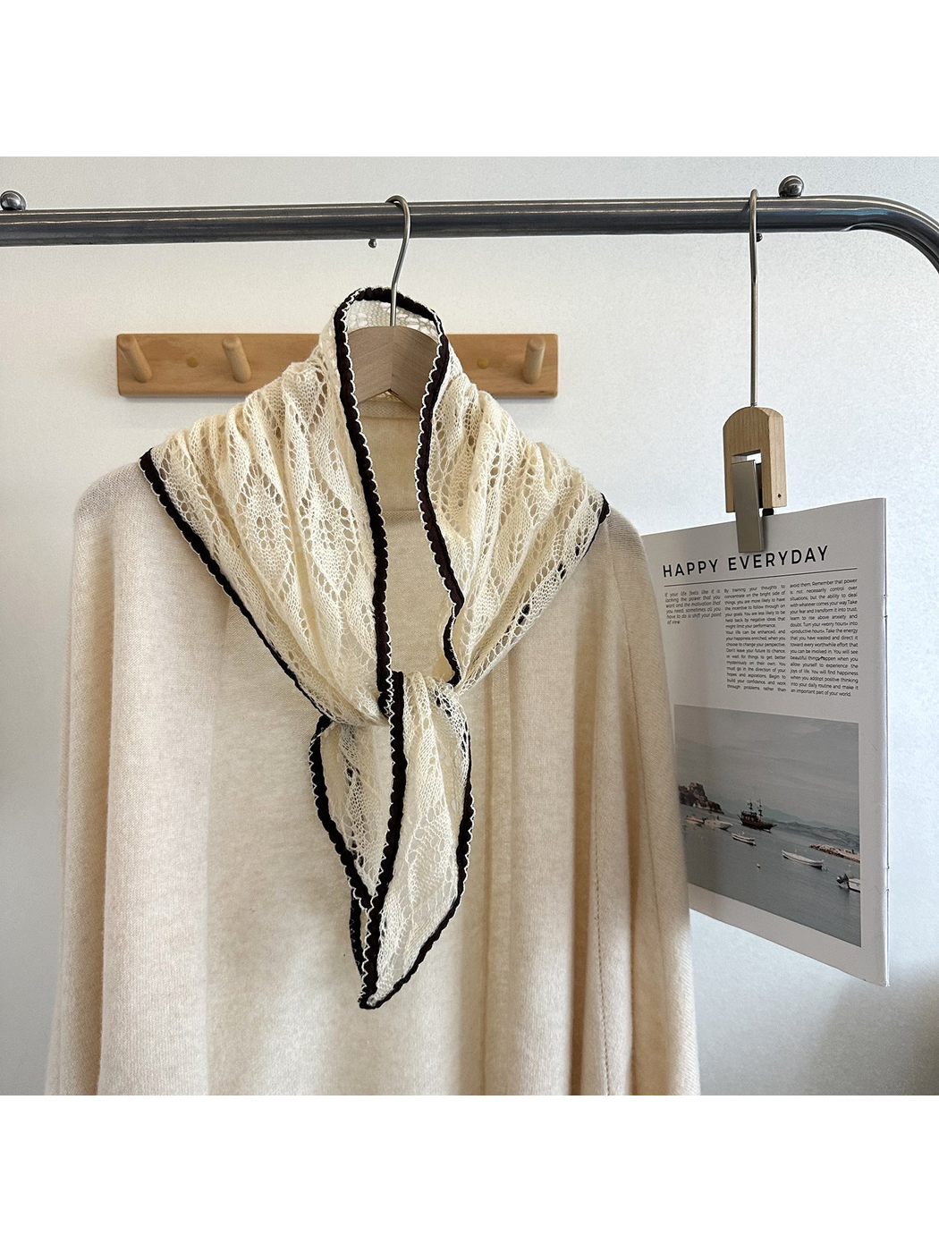 Ivory openwork tapered scarf tied over a cream top on a clothing rack