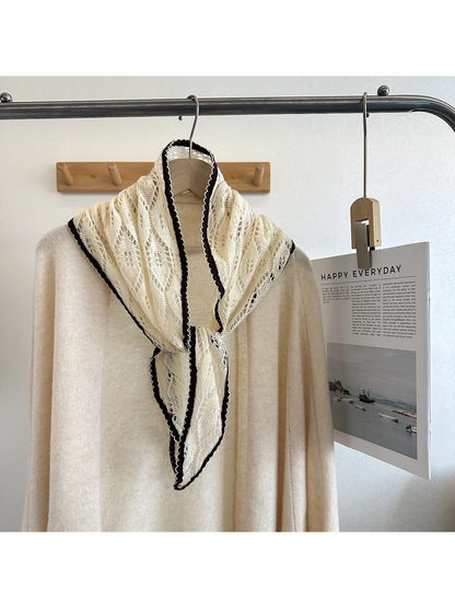 Ivory openwork tapered scarf tied over a cream top on a clothing rack
