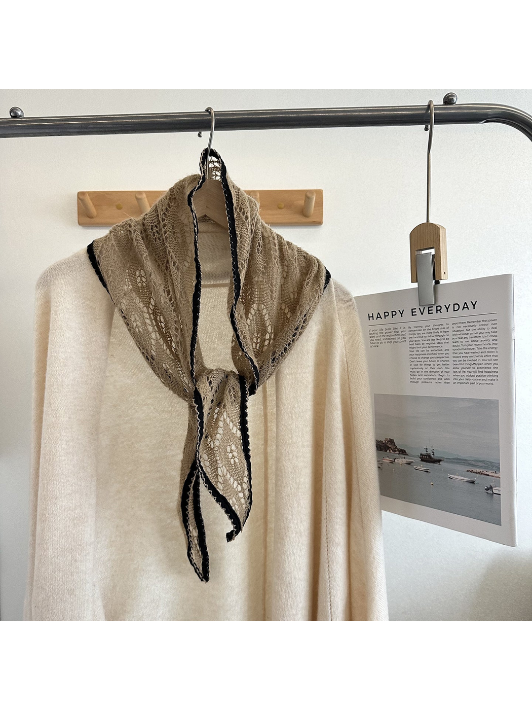 Khaki openwork tapered scarf with dark scalloped trim tied over a cream top