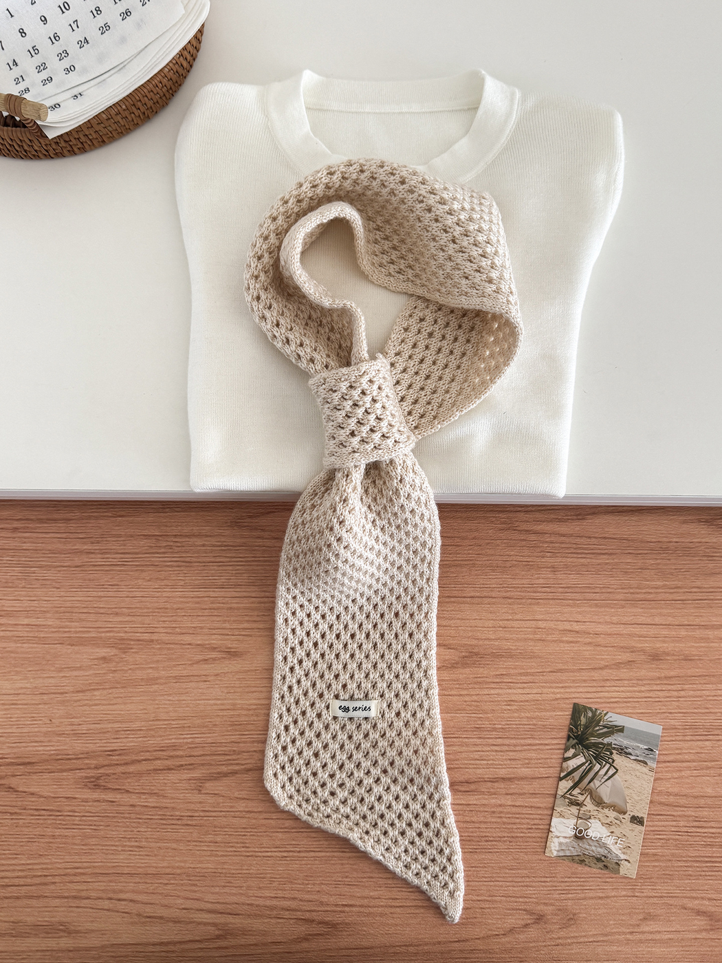 Beige openwork pull-through scarf displayed with a folded white top