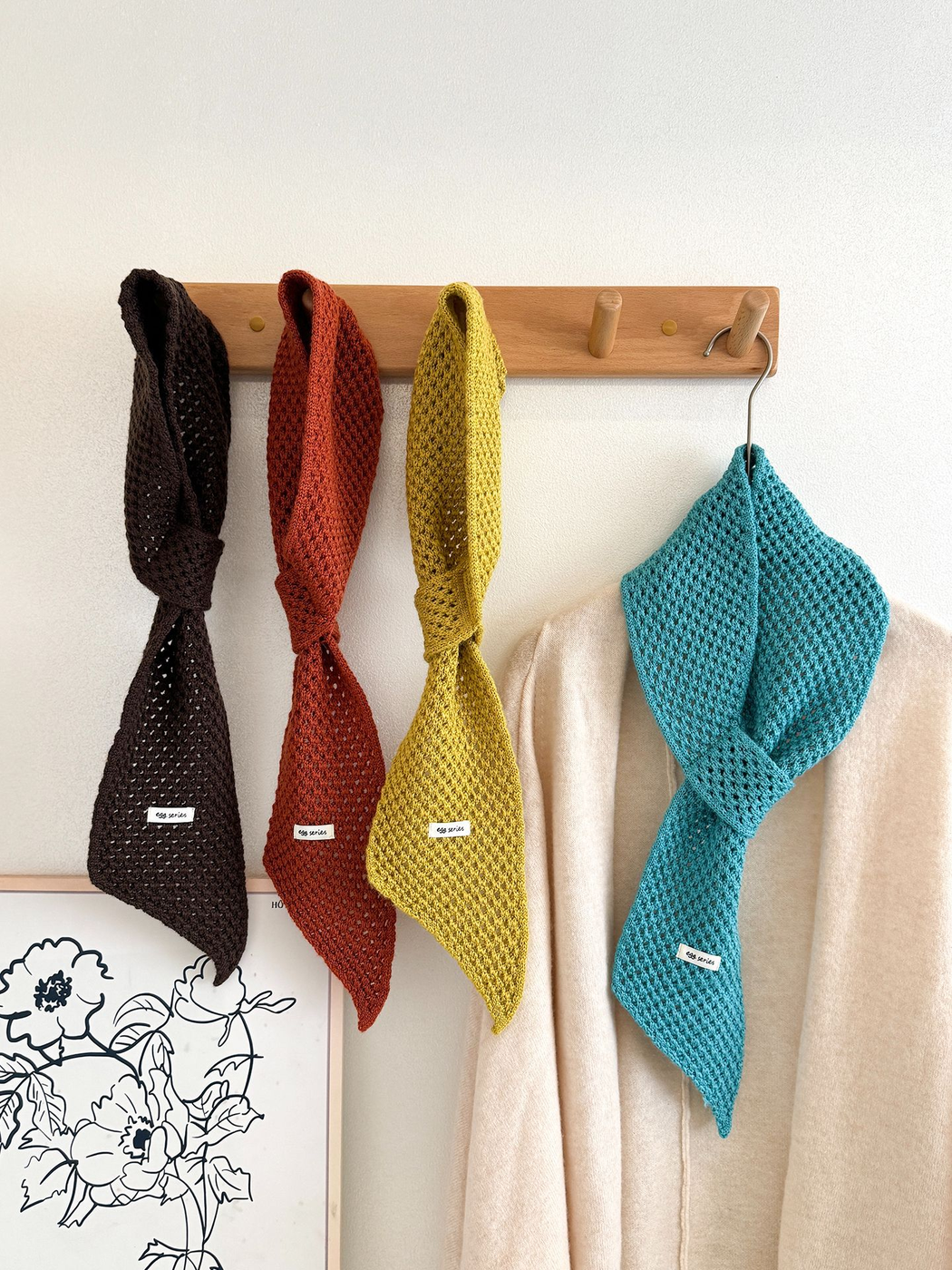 Four openwork pull-through scarves styled on a wooden wall rack