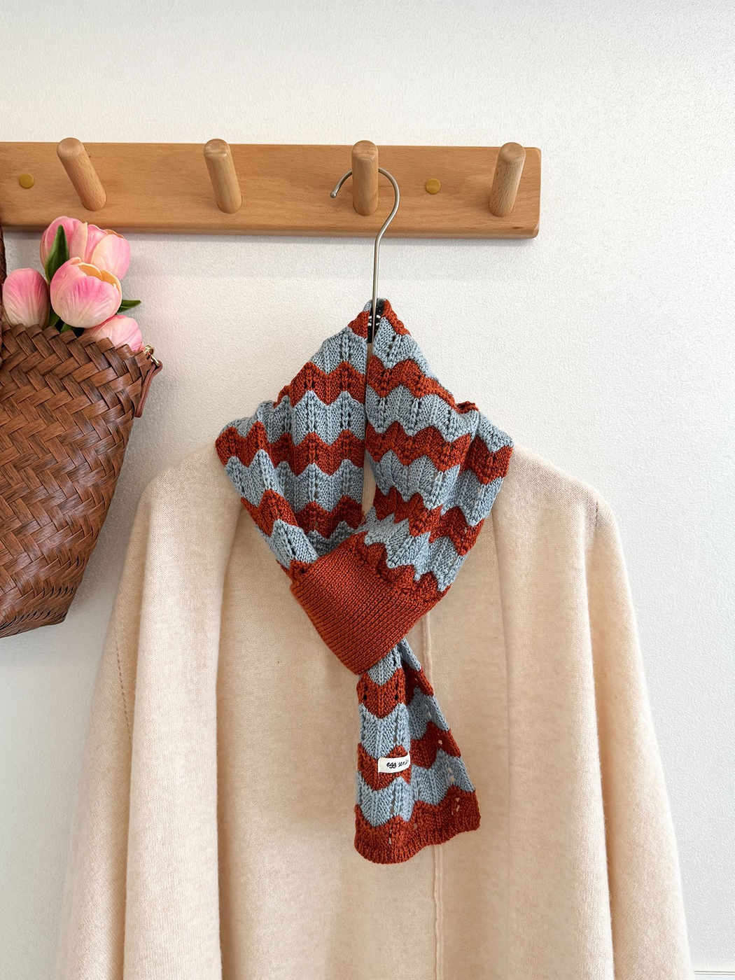 Blue and orange wavy knit pull-through scarf displayed on a hanger over a light cardigan