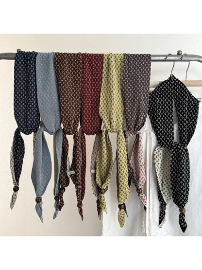 Seven color variations of the narrow patterned scarf draped on a clothing rack