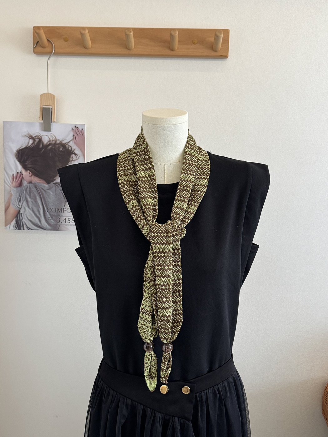 Green geometric-pattern narrow scarf styled in a long front knot on a black dress form