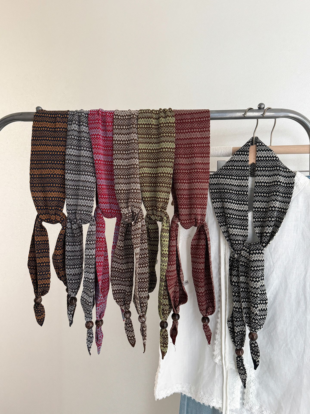 Multiple colors of the geometric-pattern narrow scarf displayed on a clothing rack