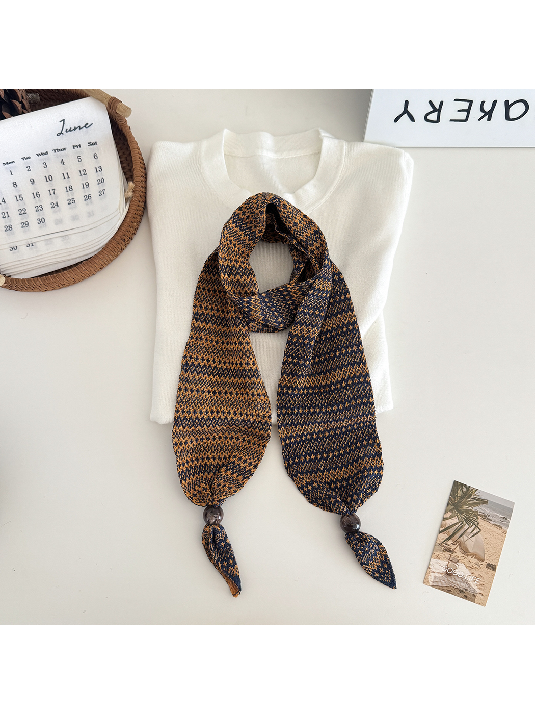 Orange geometric-pattern narrow scarf with bead accents, flat display