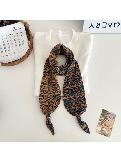 Orange geometric-pattern narrow scarf with bead accents, flat display
