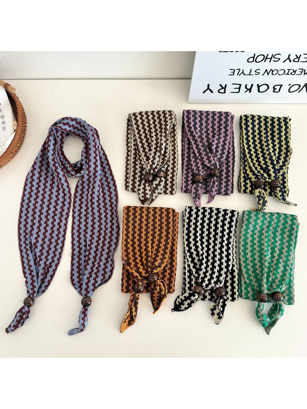 Seven color variants of the narrow patterned scarf arranged on a tabletop