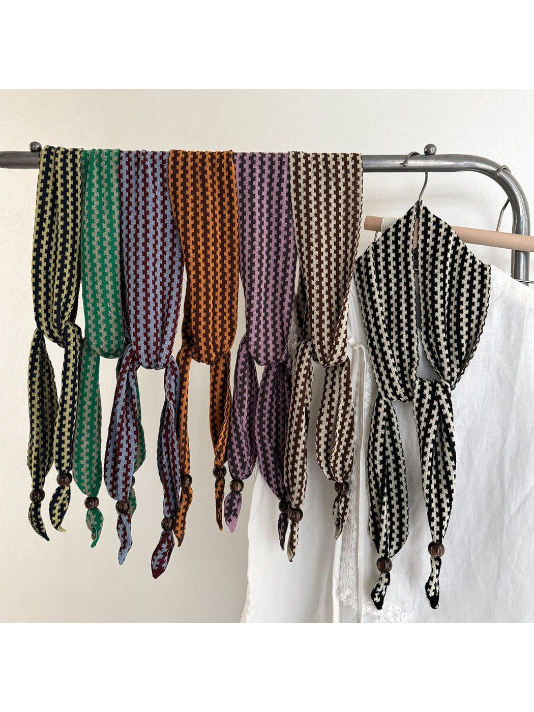 Multiple color variants of the narrow patterned scarf draped on a clothing rack