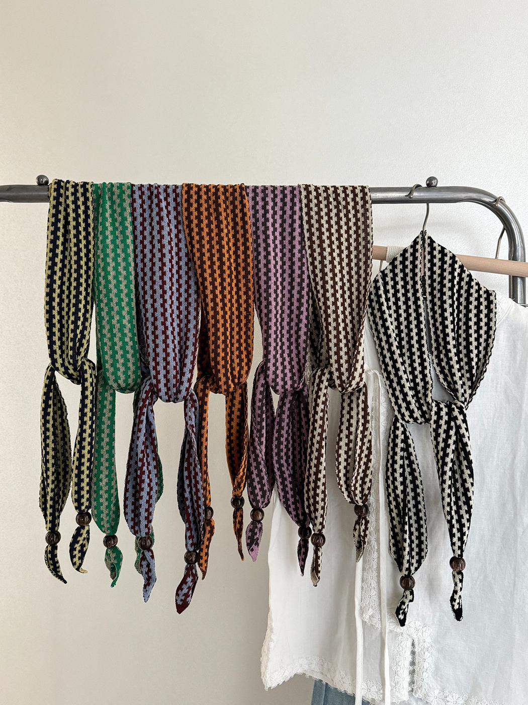 Seven color variants of the narrow patterned scarf displayed across a clothing rack