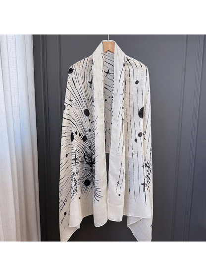Ivory-toned scarf with black abstract sunburst, line and dot pattern, fully draped on a hanger