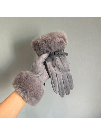 Gray gloves with furry cuffs held against a plain background
