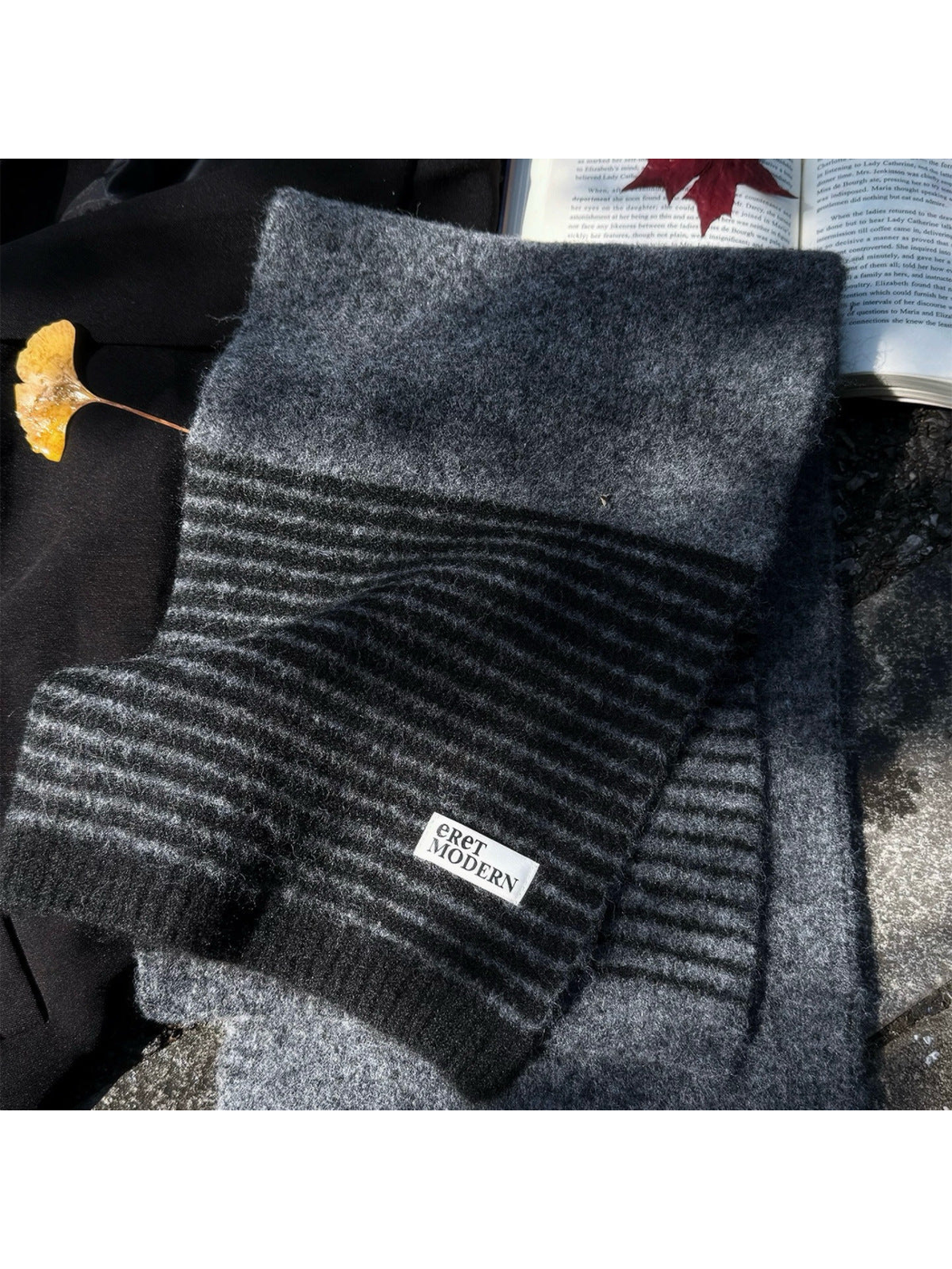 Gray striped scarf arranged beside a book and leaf