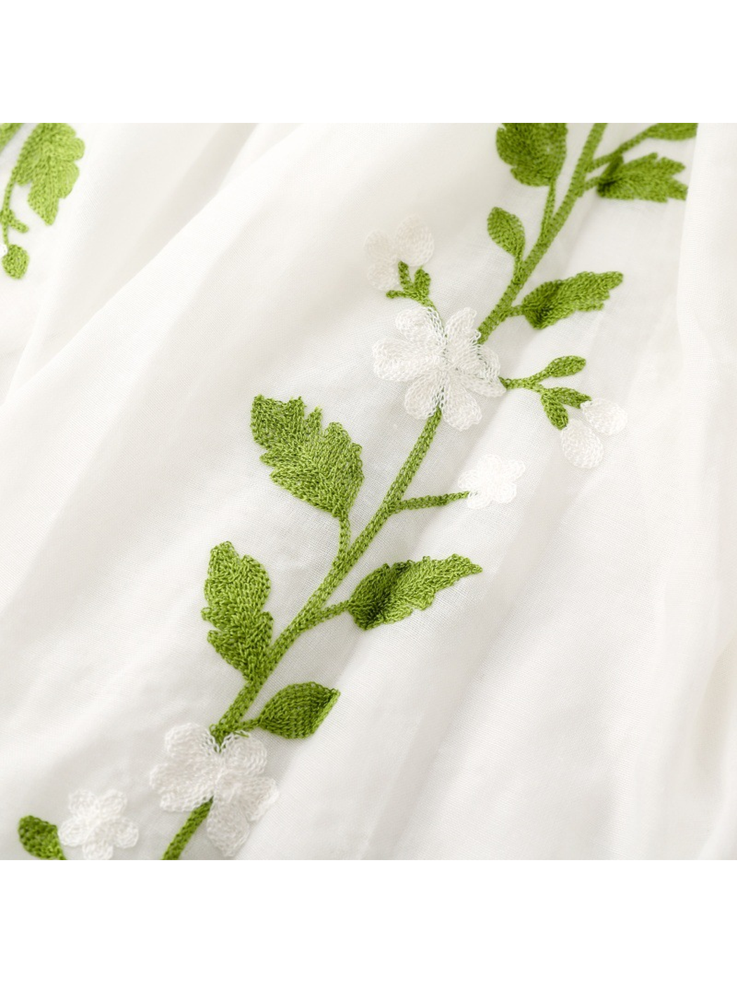 Close-up of green leaves and white floral embroidery on the White scarf