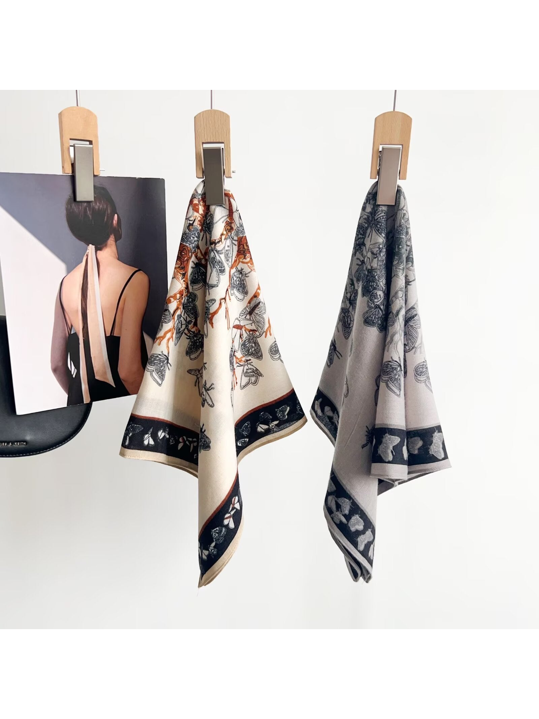 Light gray and cream butterfly-pattern square scarves displayed on hanging clips