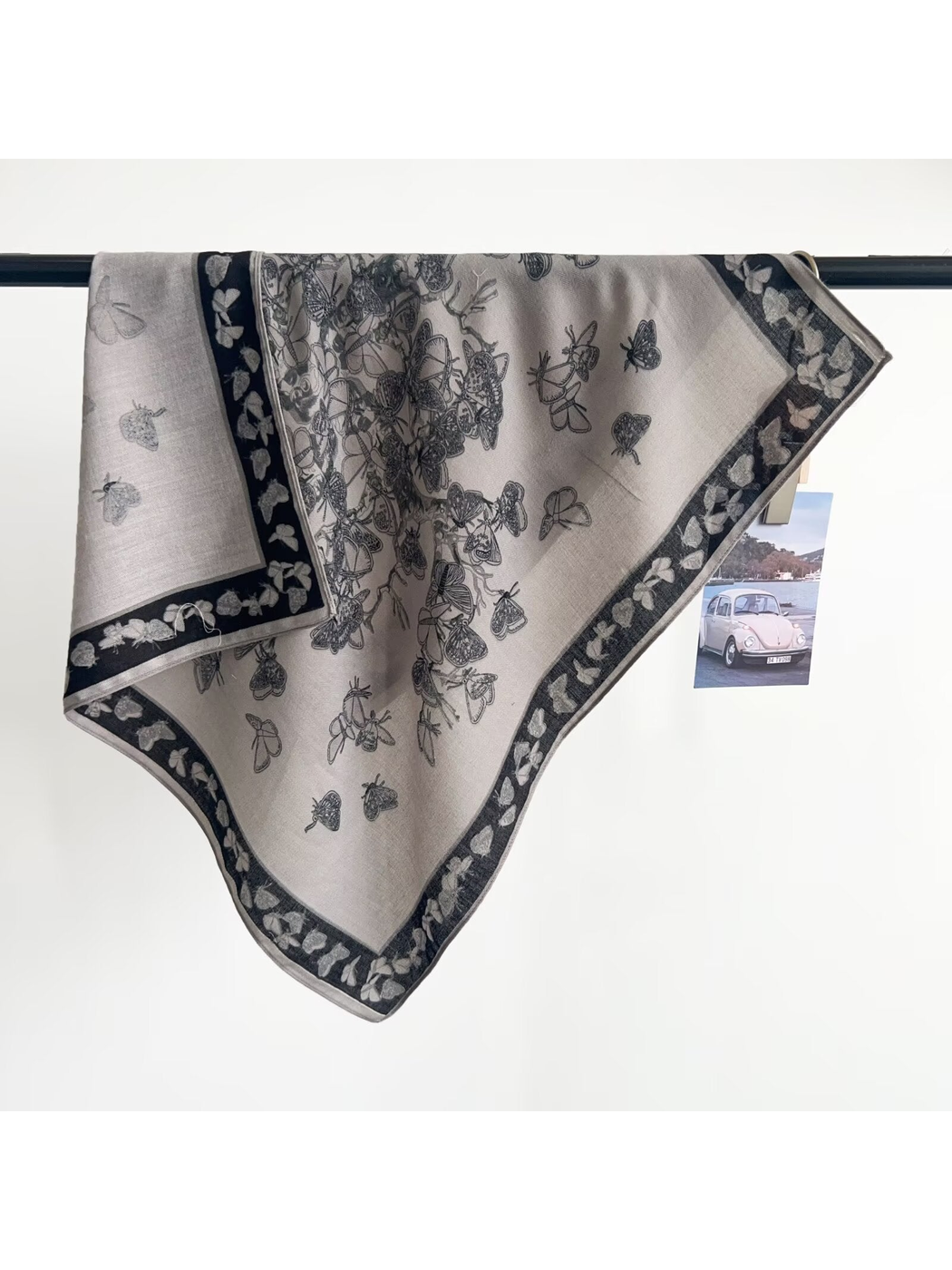 Light gray butterfly-pattern square scarf draped over a display rail