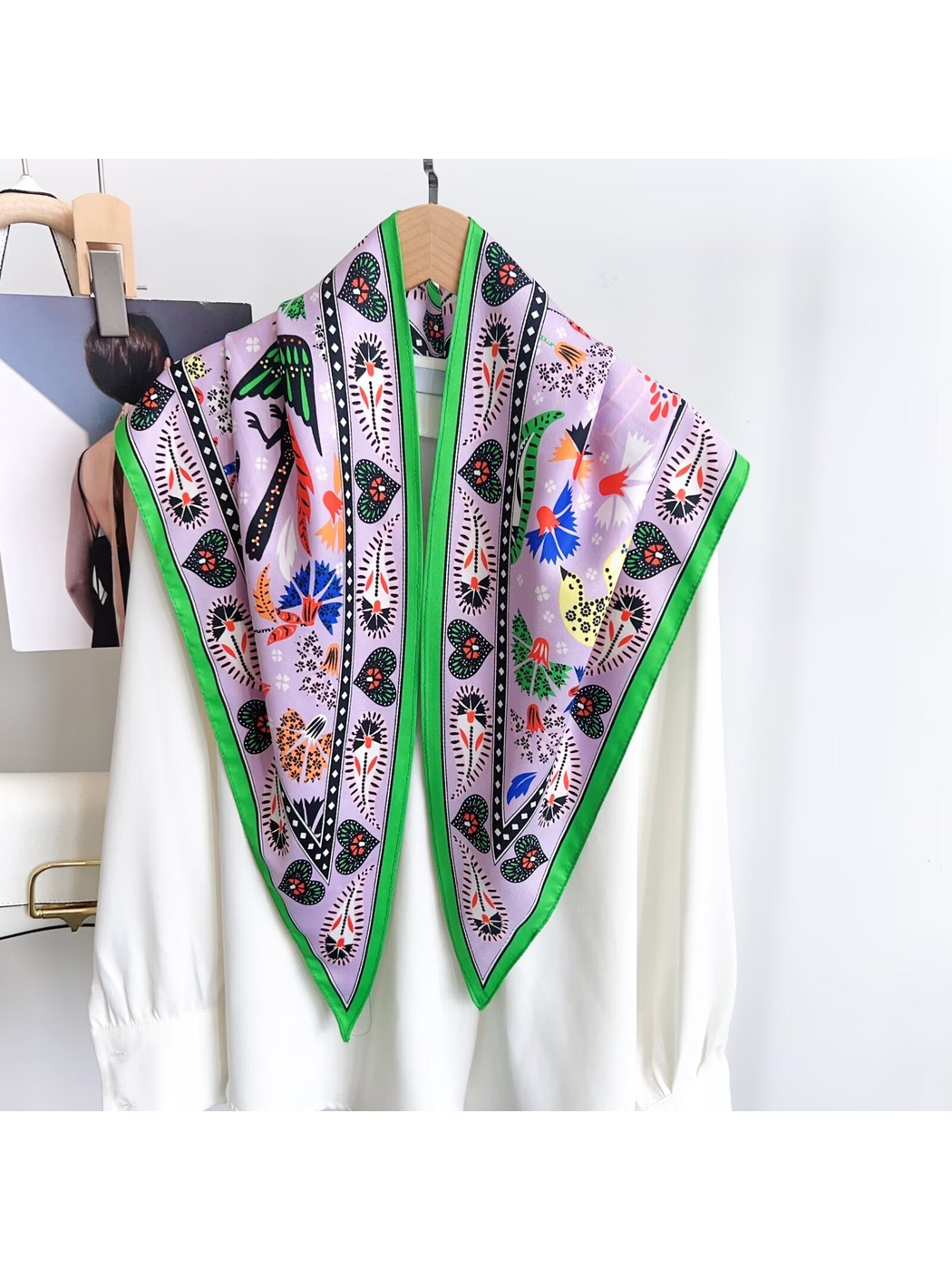 Light purple triangle scarf with green border draped over a white blouse