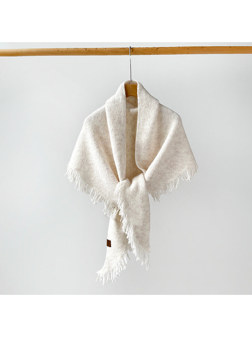 Ivory fringed scarf draped and knotted on a hanger