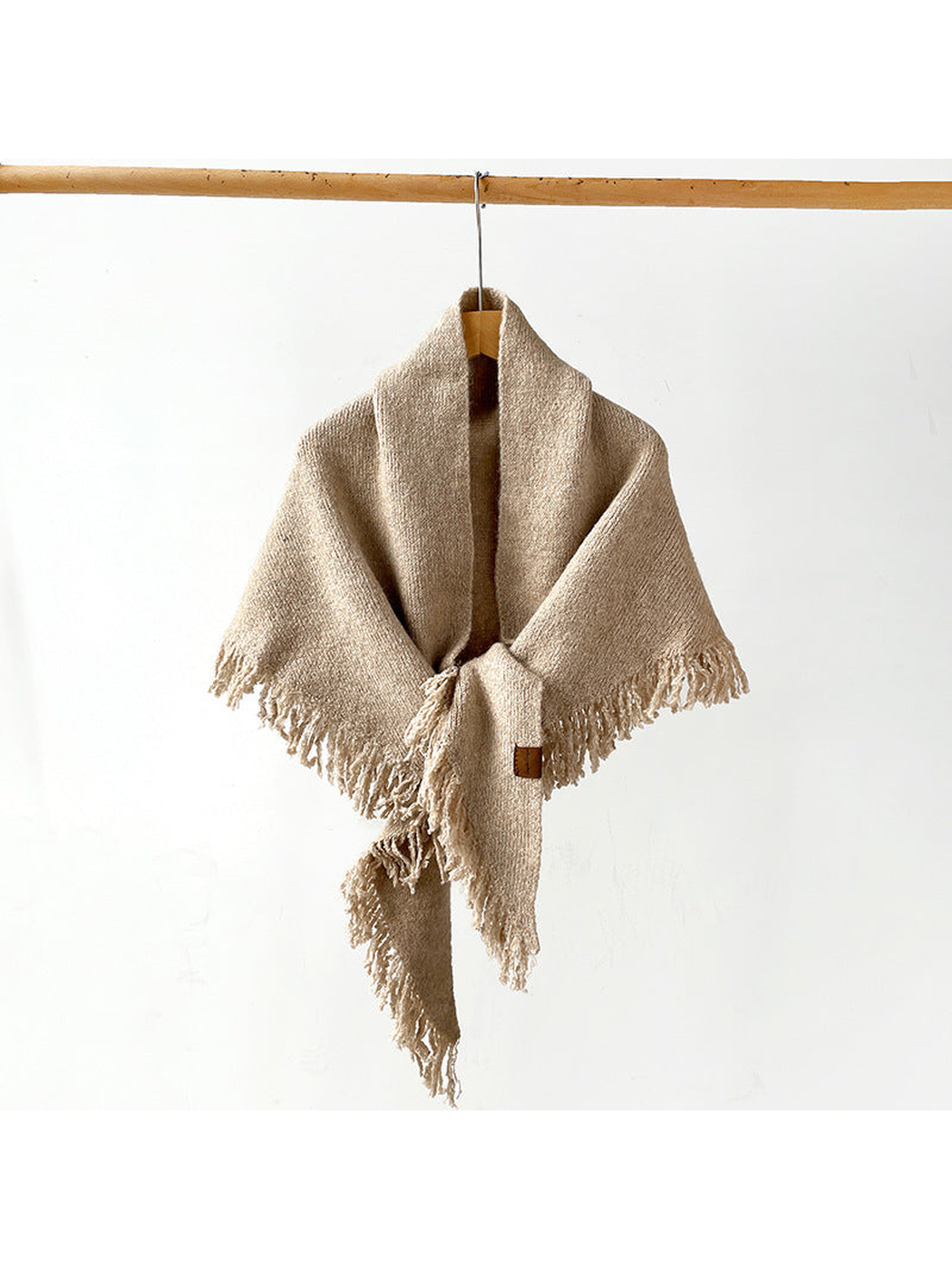 Beige fringed scarf draped and knotted on a hanger