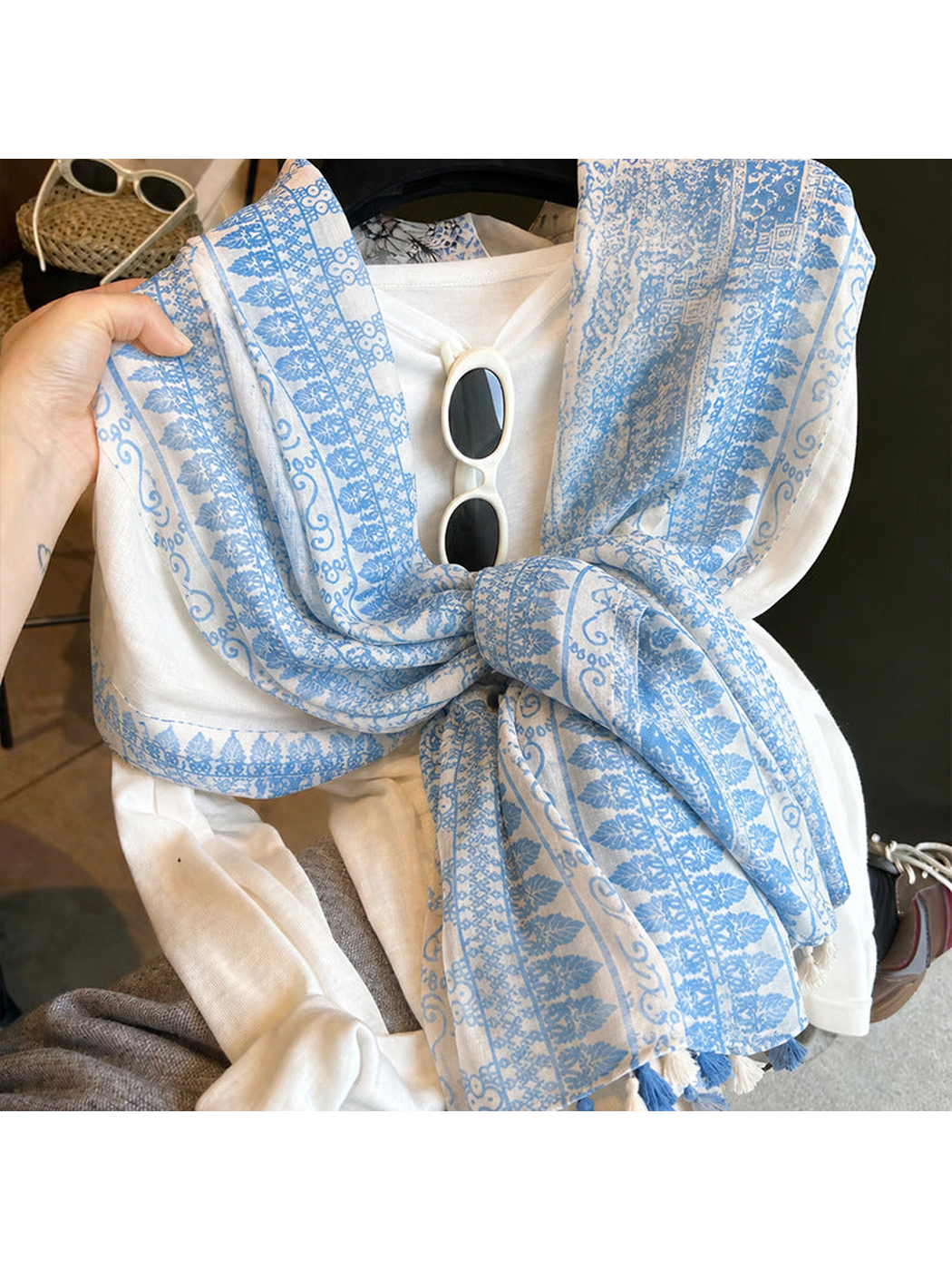 Close-up of a light blue and ivory patterned scarf tied over a white top