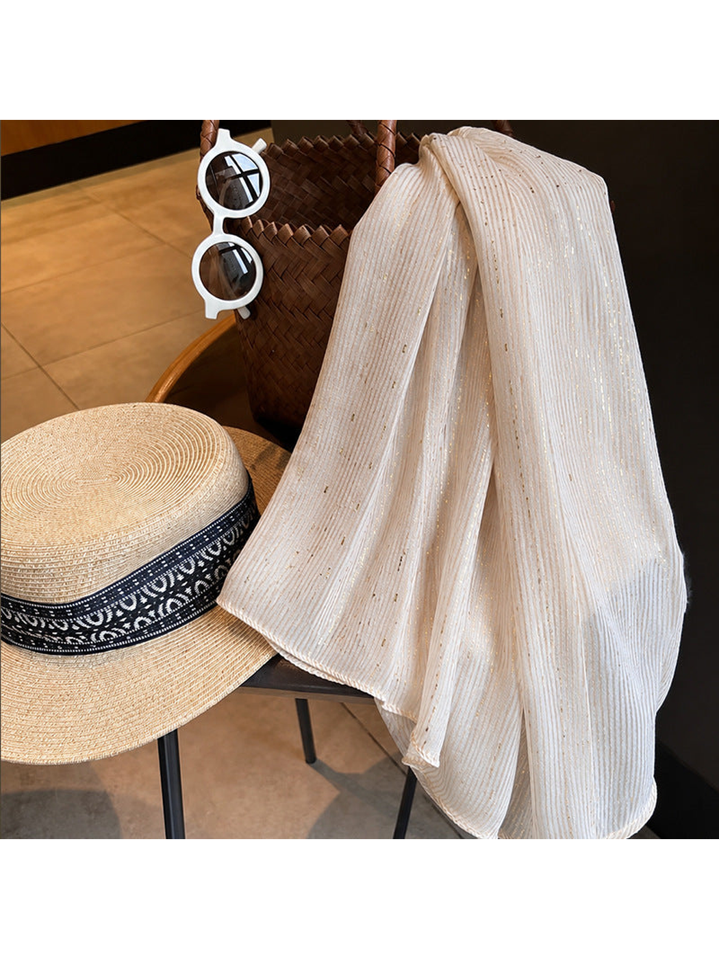 Beige pleated scarf draped over a chair beside a sun hat and woven bag