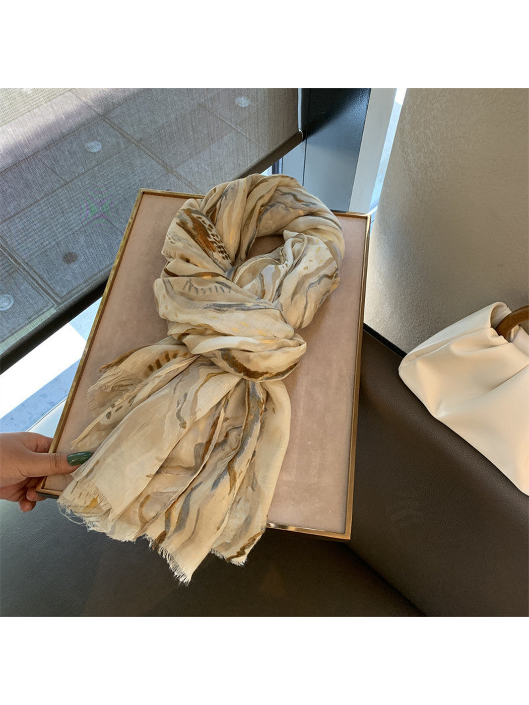 Khaki abstract-pattern scarf tied in a loose knot on a display tray