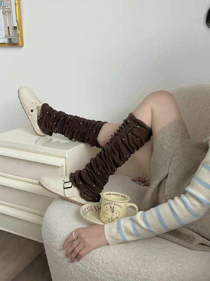 Brown polka-dot ruched leg warmers worn with white shoes in a seated crossed-leg pose