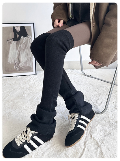 Black ribbed over-the-knee leg warmers worn with black shoes while seated