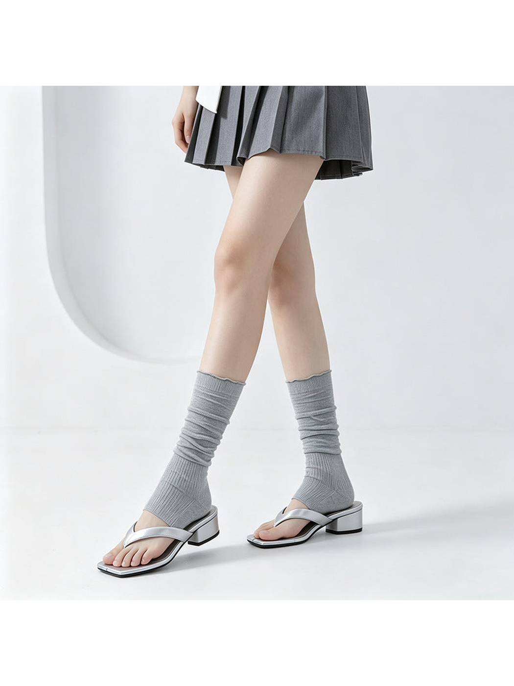 Gray ribbed open-toe mid-calf socks worn with silver sandals, standing view