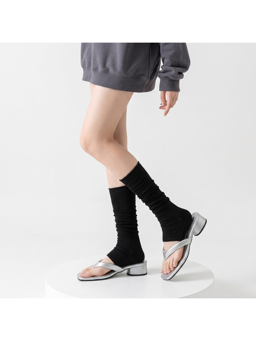 Black ribbed open-toe mid-calf socks worn with silver sandals in a standing pose