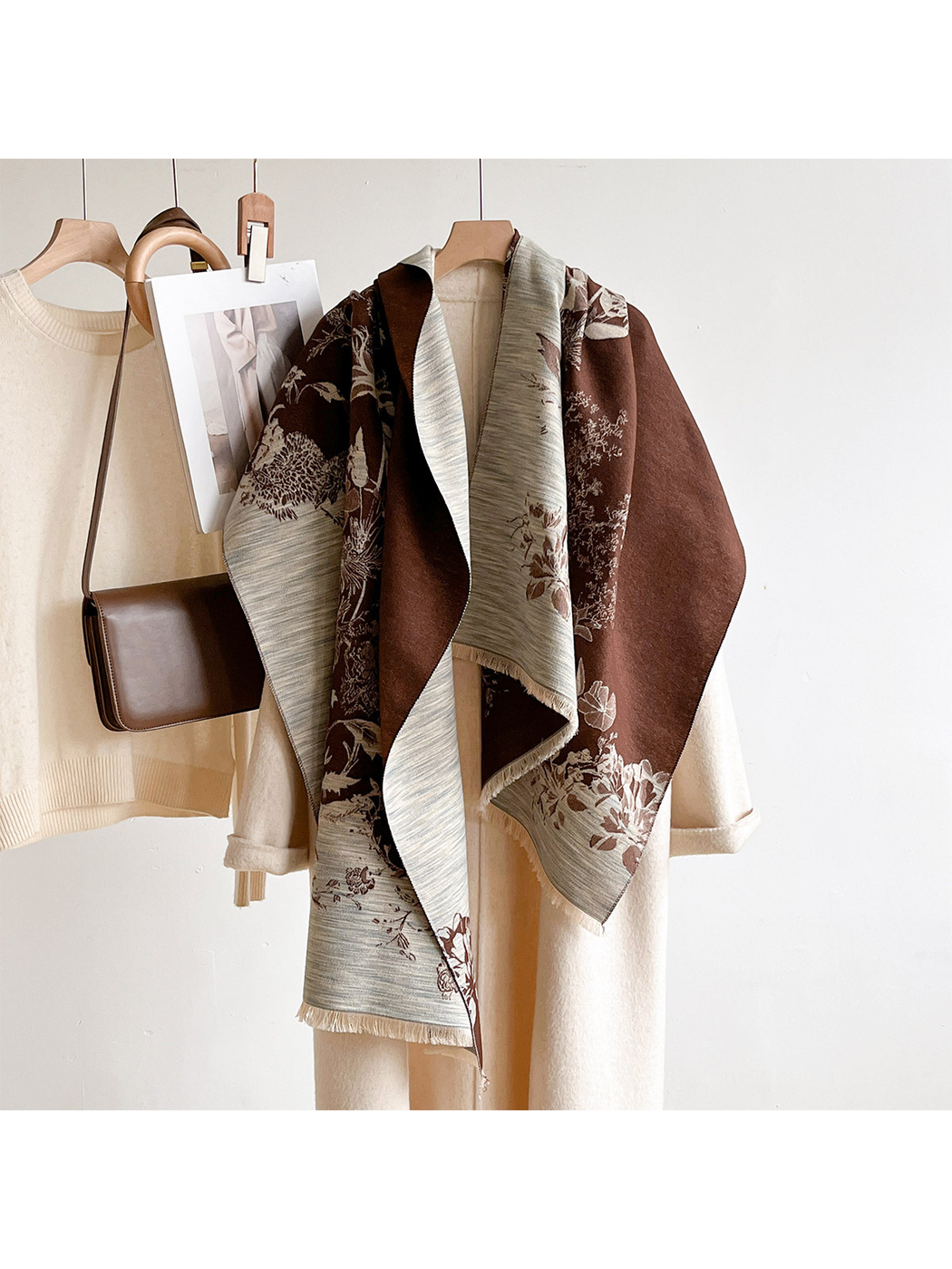 Brown floral scarf draped over a hanging ivory coat beside a sweater and brown shoulder bag.