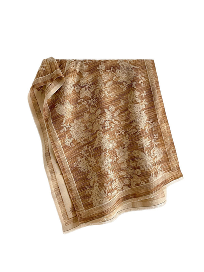 Camel scarf with cream birds and floral branches, a framed border and short fringe, draped against white.