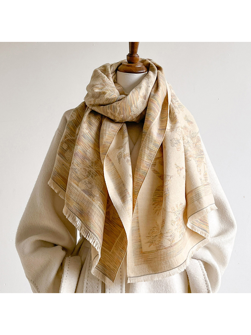 Beige bird and floral scarf looped around a mannequin's neck, with the cream reverse and fringed ends draped over a coat.