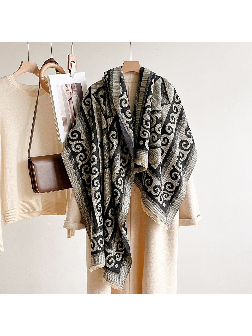 Black / Gray scroll-pattern scarf draped over a hanging cream coat beside a sweater and brown bag.