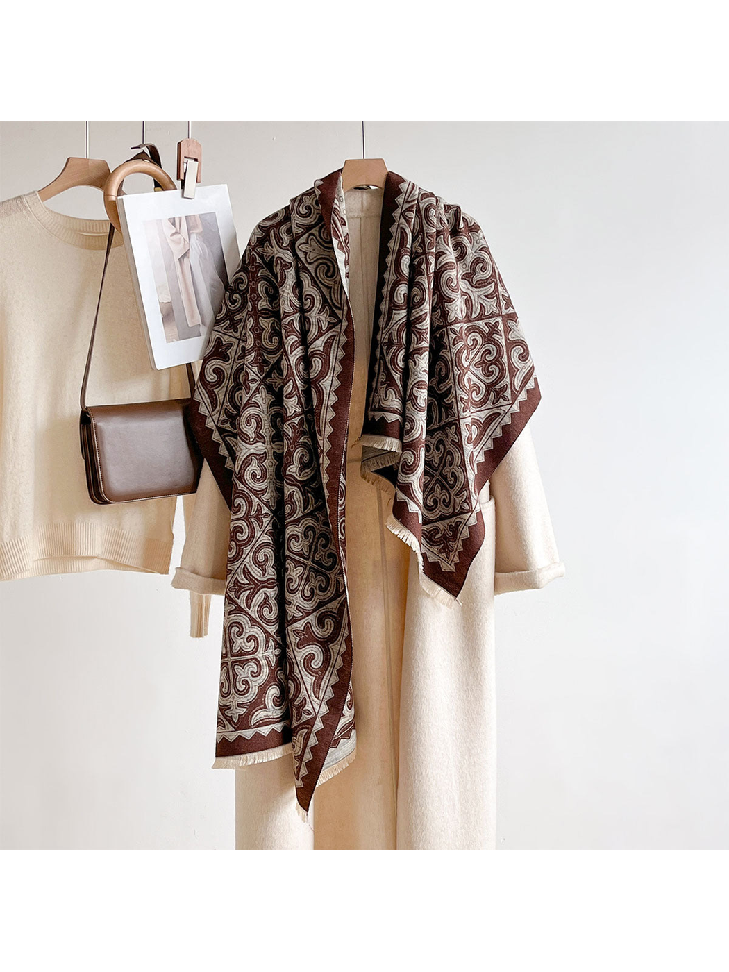 Brown ornamental scarf draped over a cream coat on a clothing rack