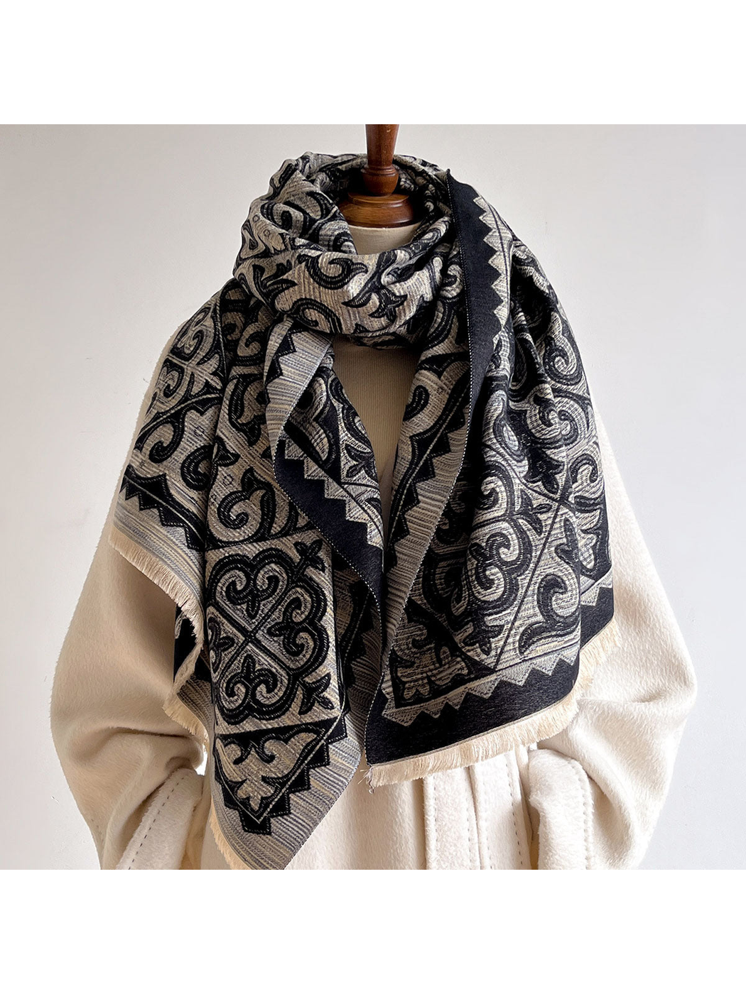 Dark ornamental scarf looped around a mannequin over a cream coat