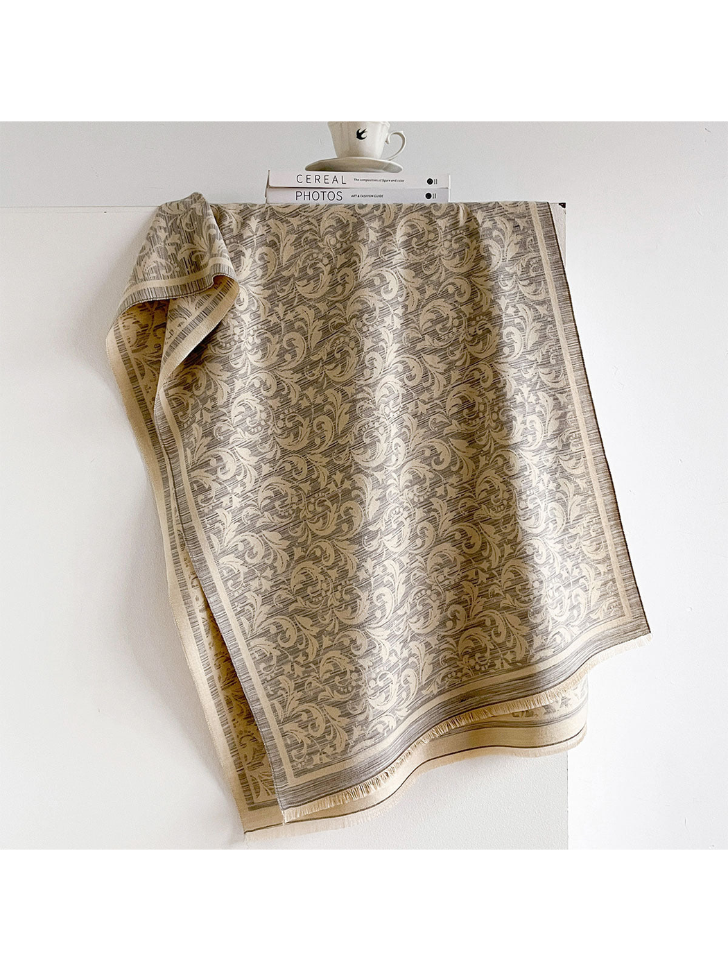 Light Gray scarf with cream scrolling leaves, a striped border and short fringe, draped open.